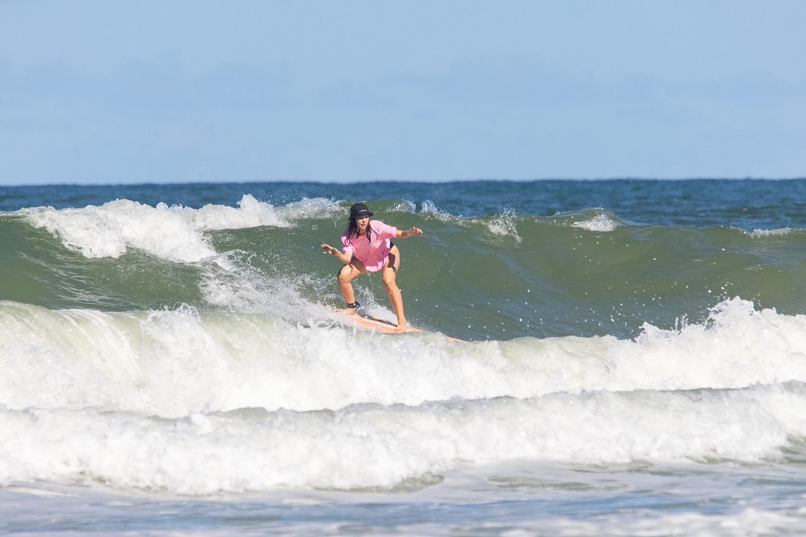 Participante surfando uma onda durante a aula na Praia da Engenhoca